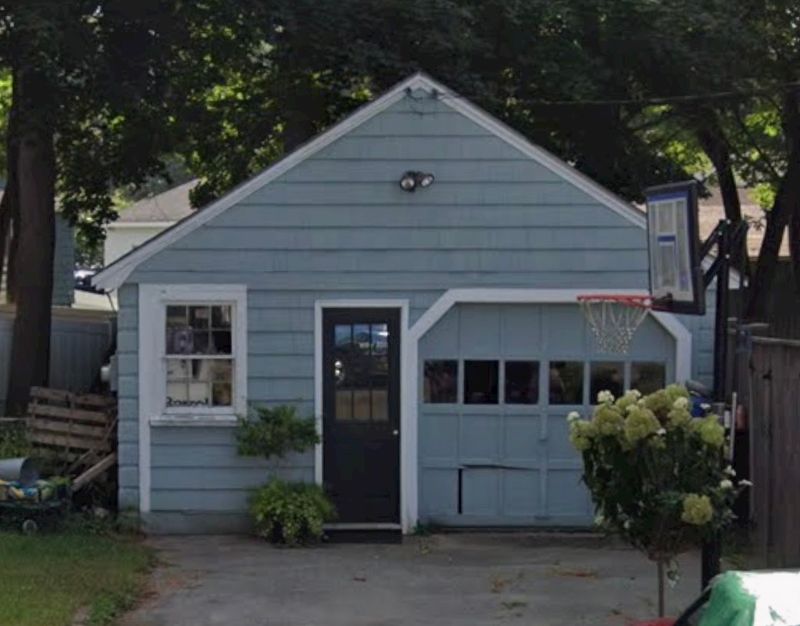 Charming blue cottage with carriage-style garage door and garden landscaping