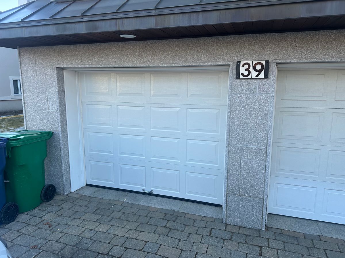 Older white raised-panel garage door before replacement on stone-faced home exterior